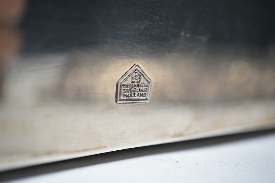 A Thai white metal cigarette box, wood lined, stamped Thainakon, 20cm and a Ceylonese white metal dish, shaped in the form of the country, with embossed borders, and inscription, maker’s mark SS, 24.7cm long, 182g. Condi